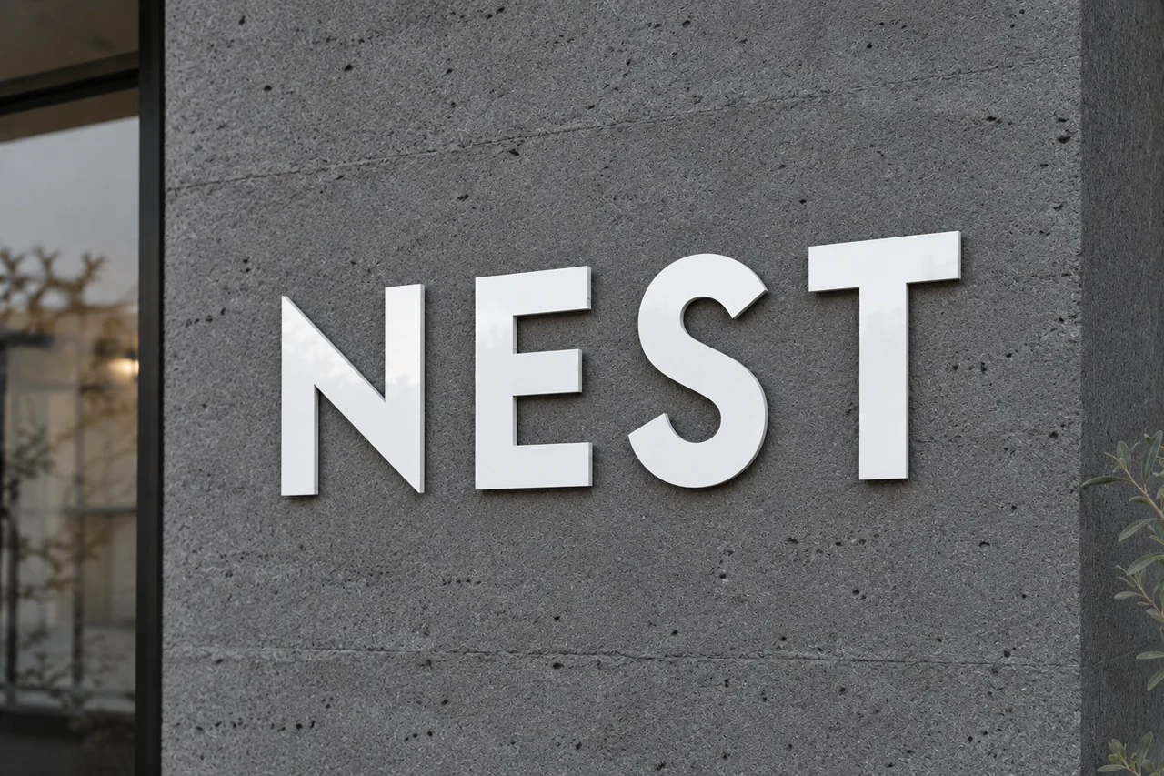 グレーの壁面に取り付けた薄い白いNESTのアルミ複合板文字