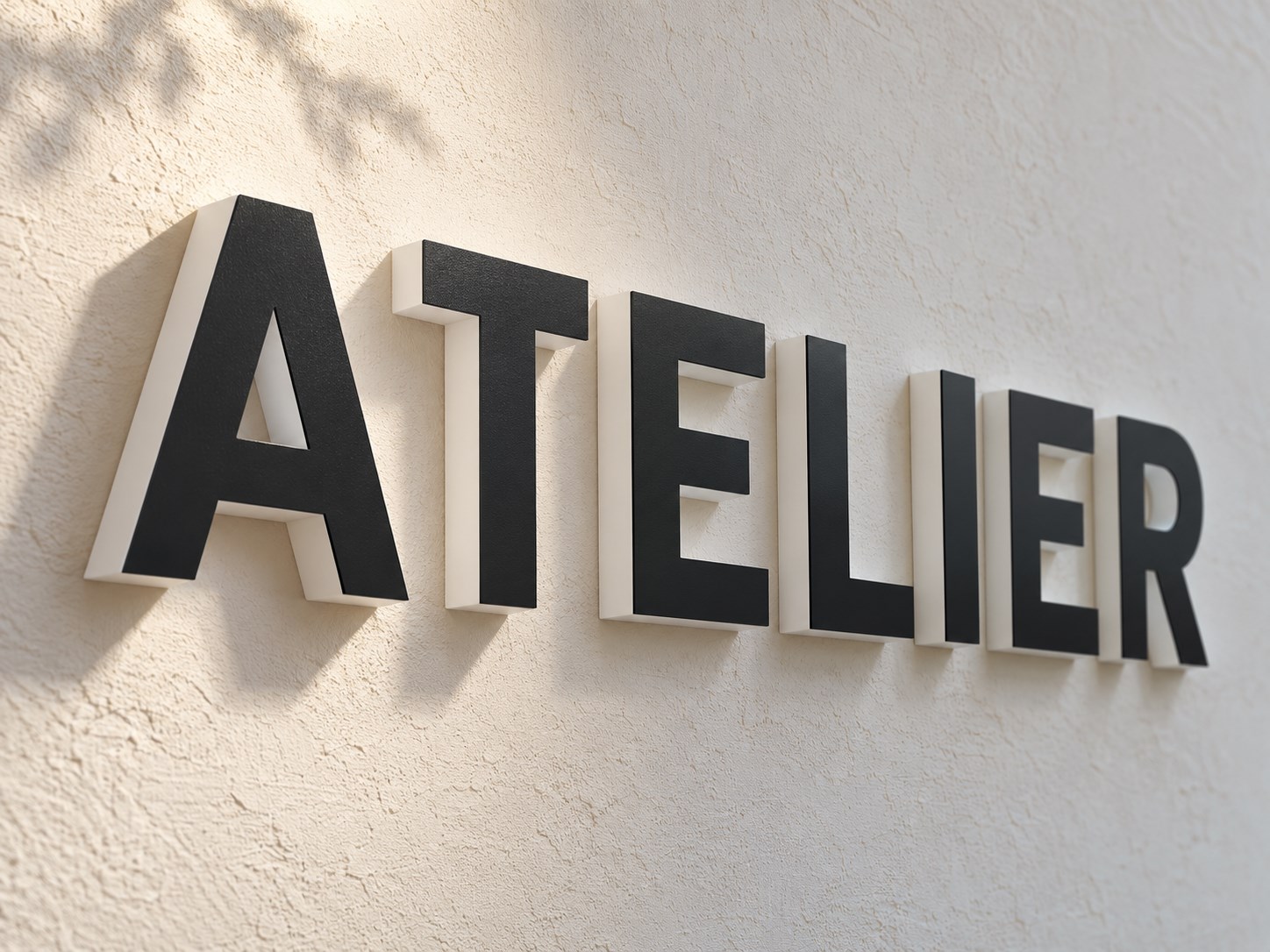 白い壁のATELIERのカルプ文字を斜めから見た写真。黒い表面と白い側面の厚みが分かる